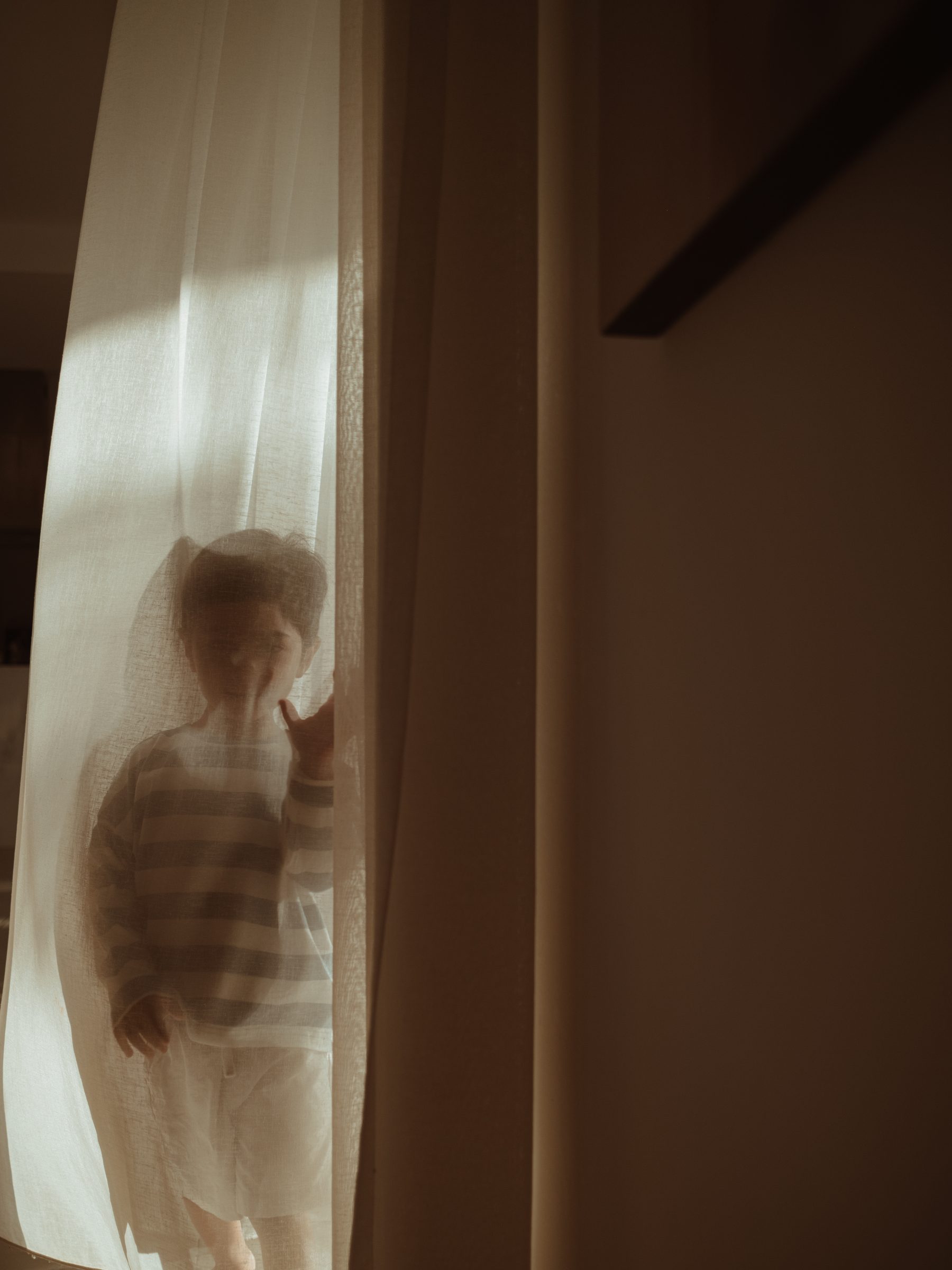 Child behind a sheer curtain in soft light